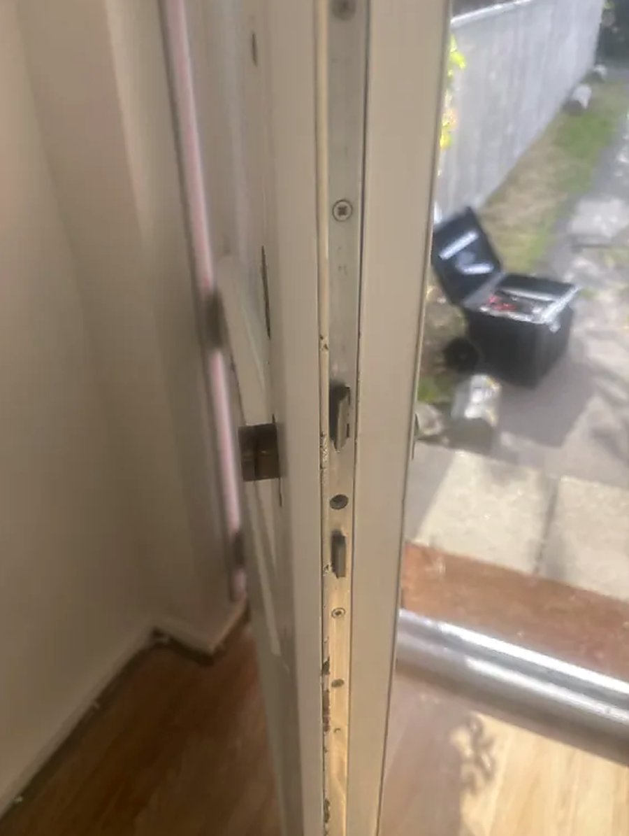 Edge of a uPVC front door showing the multipoint lock strip, hook and keeps, with a locksmith's tool case on the path outside