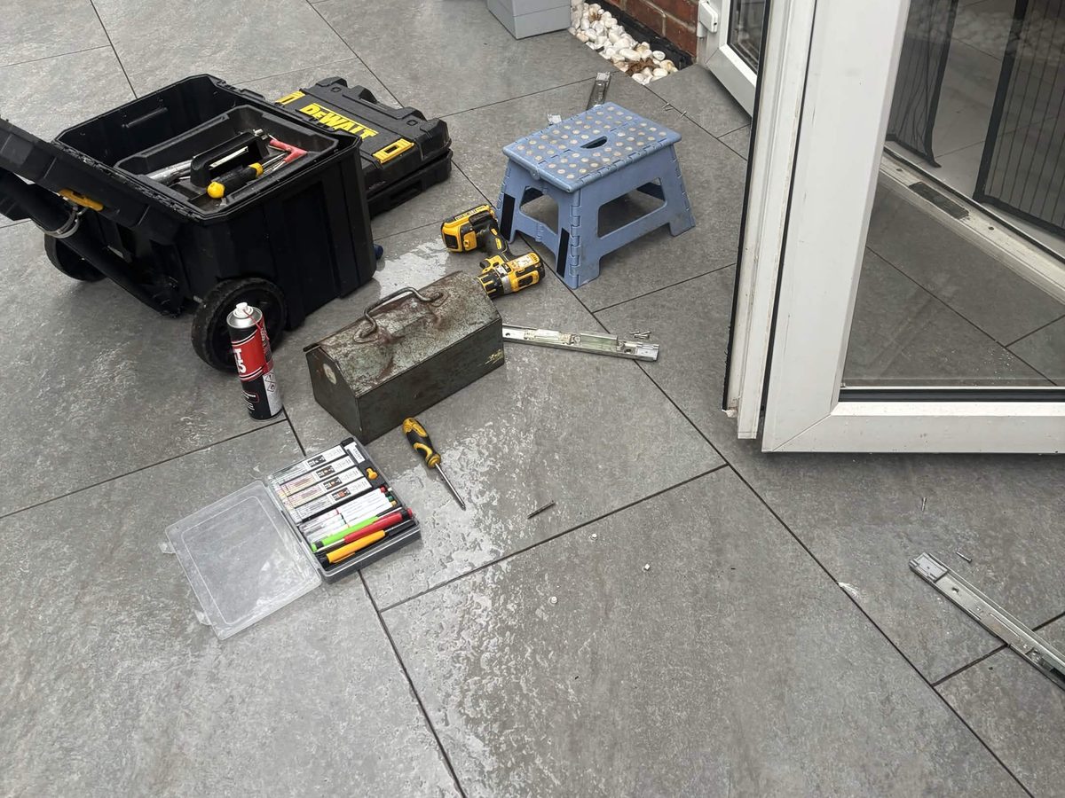 Parts taken off a uPVC French door laid on the patio beside a toolbox, drill and spray can